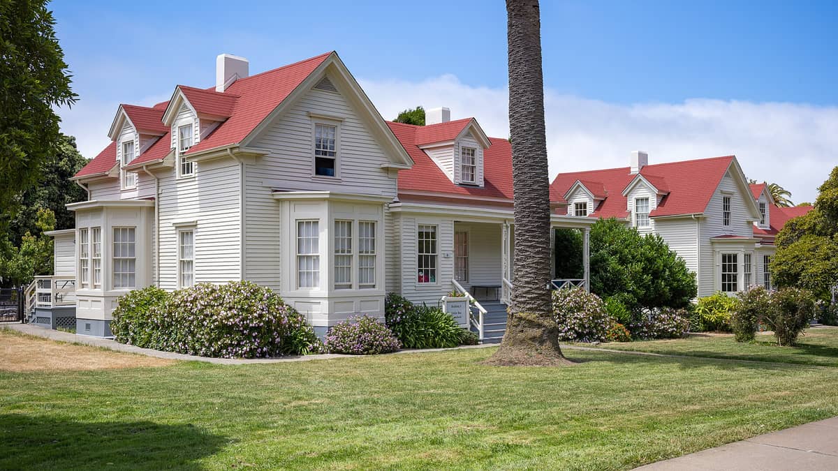 Casas históricas de oficiales del Presidio, de color blanco con distintivos techos rojos y abundante vegetación, rodeadas de praderas verdes bajo un cielo azul en el parque del Presidio de San Francisco.