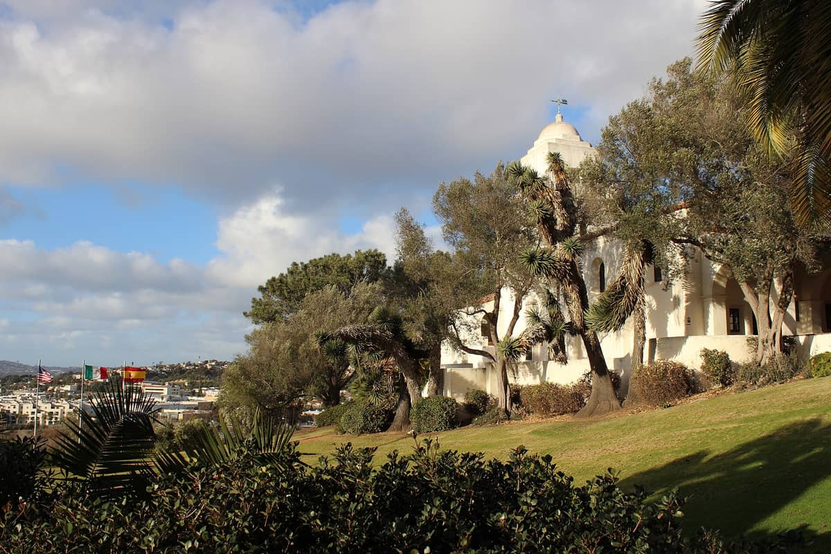 Panoramablick auf die gepflegten Grünflächen des Presidio Parks mit dem weißen Serra Museum, alten Bäumen und dem Hügelhang mit Aussicht auf Old Town und die Stadt.