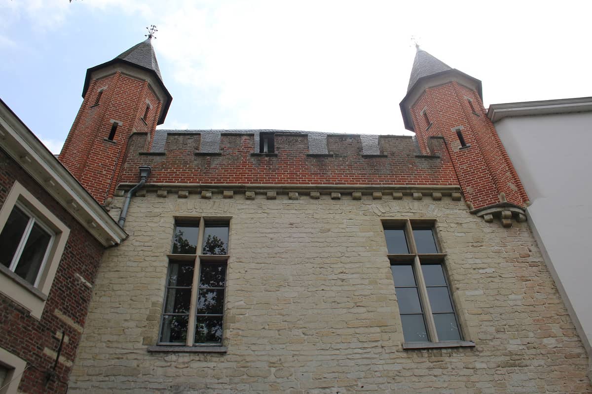 View of the surviving Prinsenhof palace gate in Ghent with two red brick towers and crenellated wall section between them.