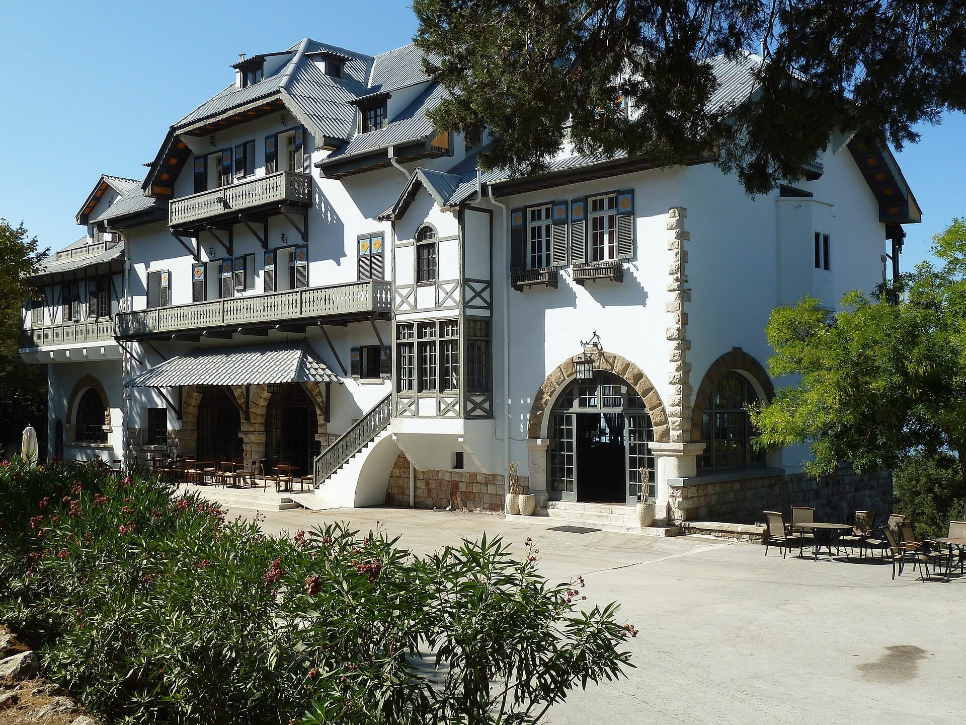 อาคารประวัติศาสตร์สมัยอิตาลีที่ Profitis Ilias เกาะ Rhodes ล้อมรอบด้วยต้นไม้เขียวชอุ่มและที่นั่งกลางแจ้งใต้ท้องฟ้าสีฟ้าใส