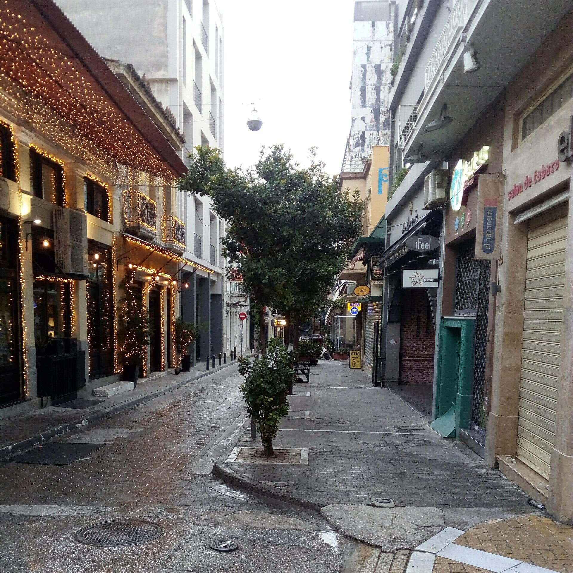 ถนนแคบในย่าน Psyrri กรุง Athens พร้อมอาคารนีโอคลาสสิกที่ตกแต่งสวยงาม ไฟประดับระยิบระยับ และทางเดินร่มรื่นในวันที่เงียบสงบ