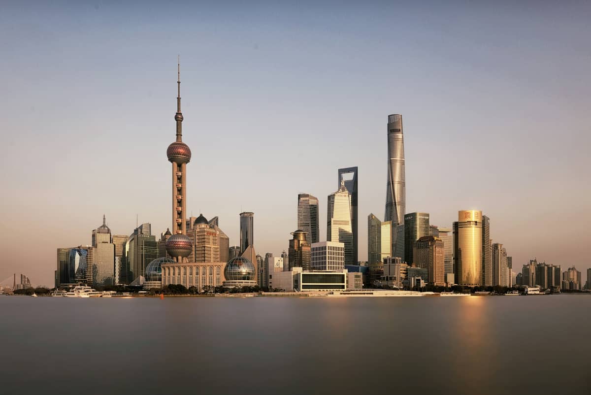 Panoramablick auf Pudongs ikonische Skyline mit dem Oriental Pearl Tower, dem Shanghai Tower und weiteren Wolkenkratzern, die sich bei Sonnenuntergang im Huangpu River spiegeln.
