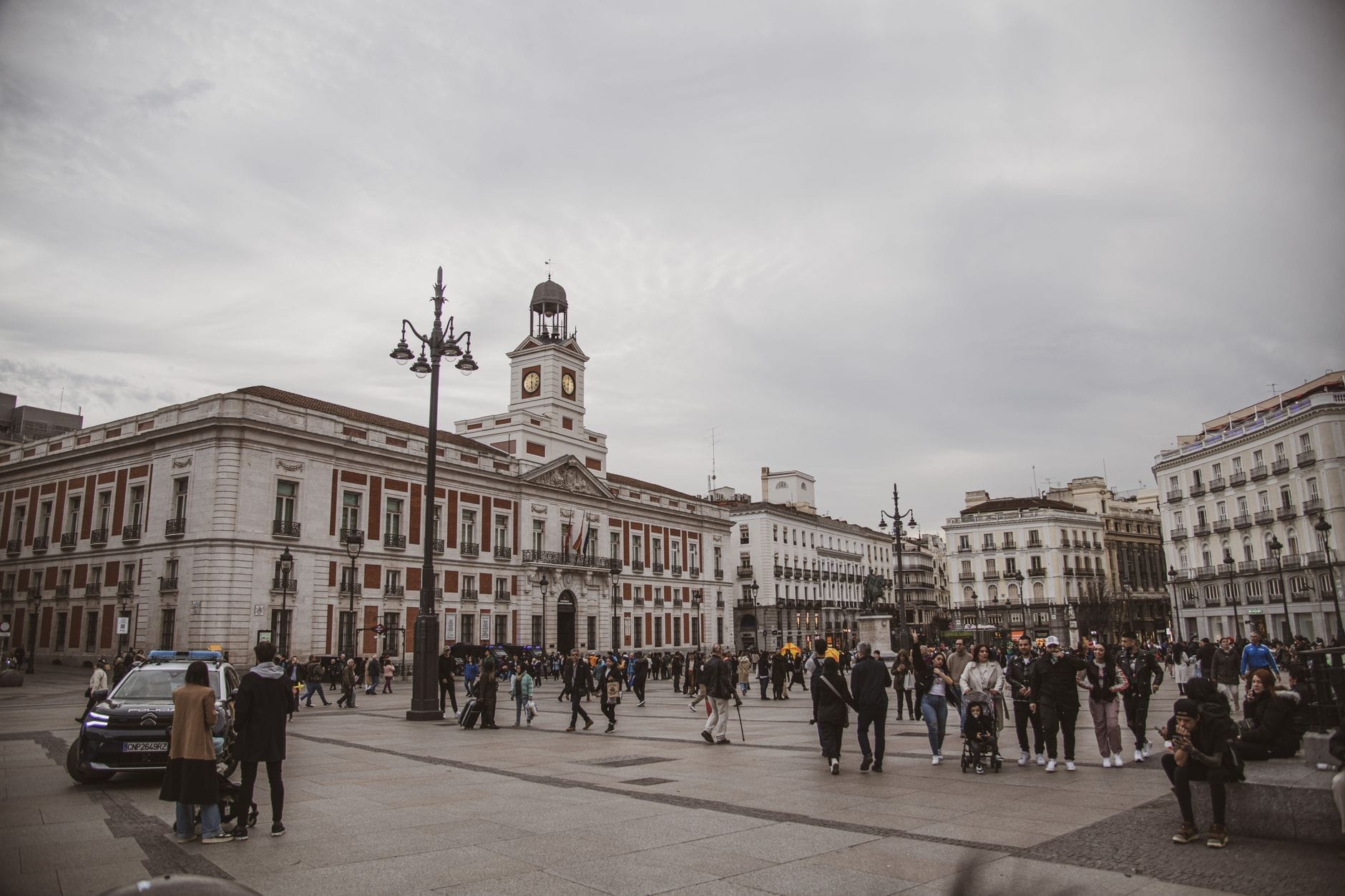 Vista panoramica di Puerta del Sol a Madrid con la torre dell'orologio della Real Casa de Correos e la folla in una giornata nuvolosa.