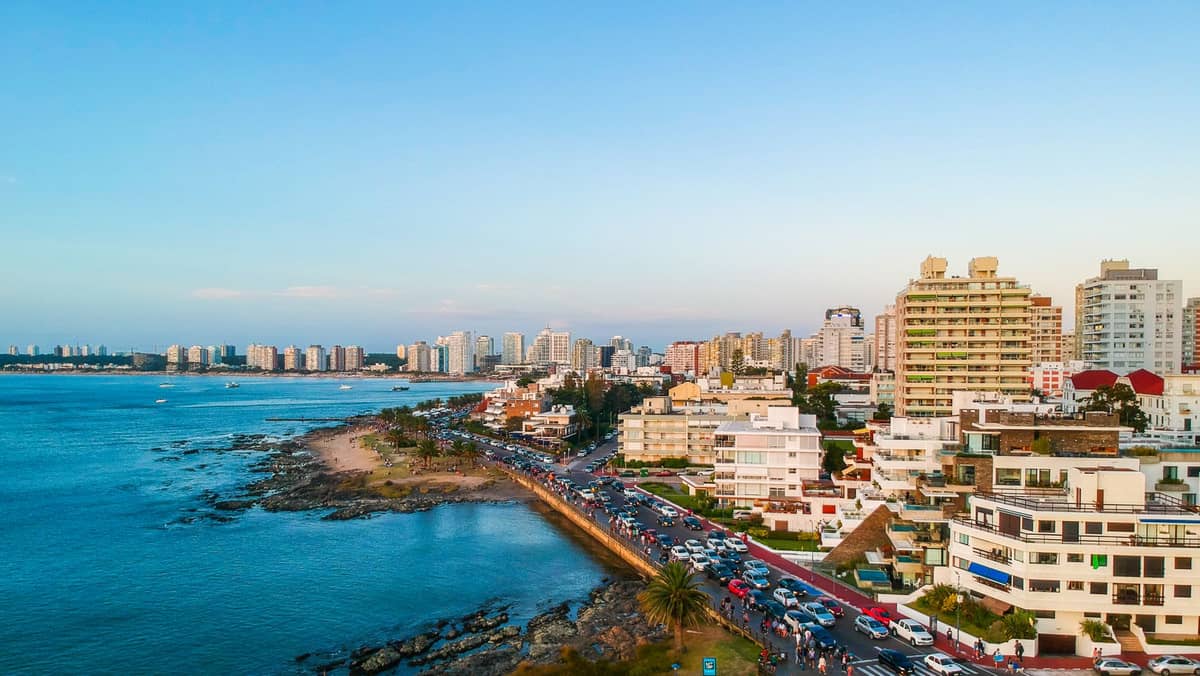 ภาพมุมสูงของแนวชายฝั่ง Punta del Este มีตึกสูงสมัยใหม่ ชายฝั่งหินและทะเลสีน้ำเงินภายใต้ท้องฟ้าแจ่มใสยามพระอาทิตย์ตก