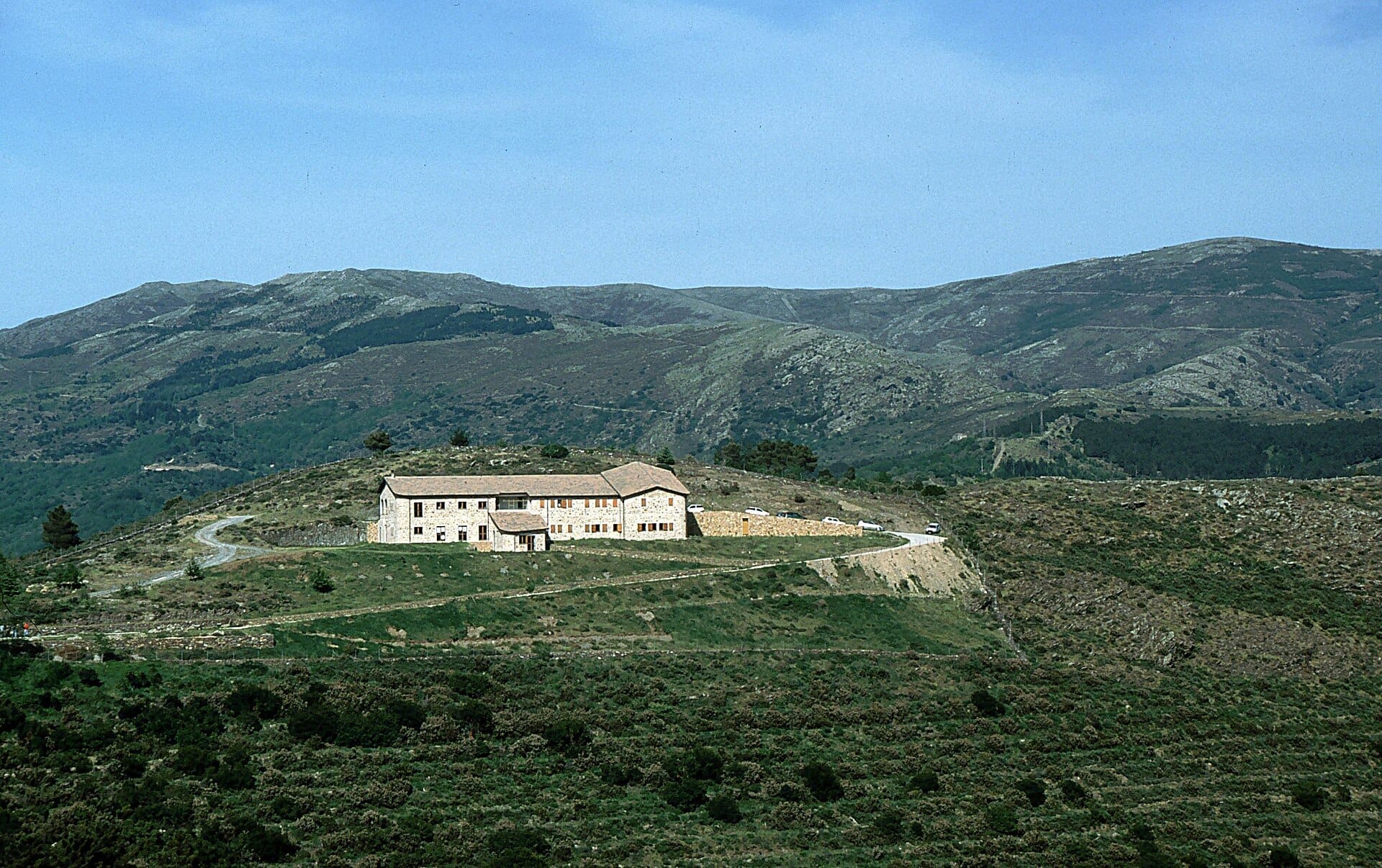 Steinhütte umgeben von kurvenreichen Straßen und zerklüfteten grünen Hügeln bei Punta La Marmora, mit den Gennargentu-Bergen im Hintergrund.