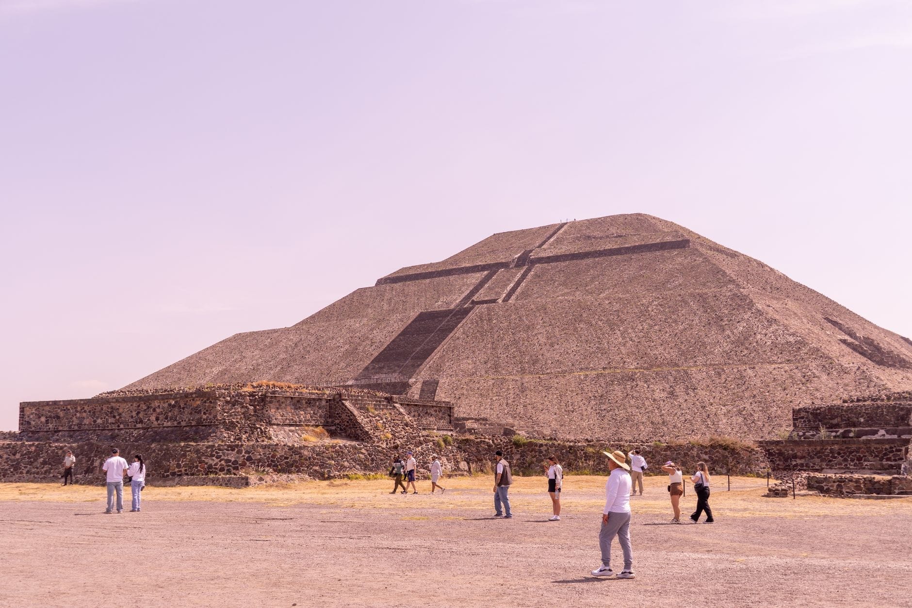 Vista panoramica della Piramide del Sole a Teotihuacan sotto un cielo limpido, con visitatori che camminano in primo piano: l'imponenza del monumento è immediata.