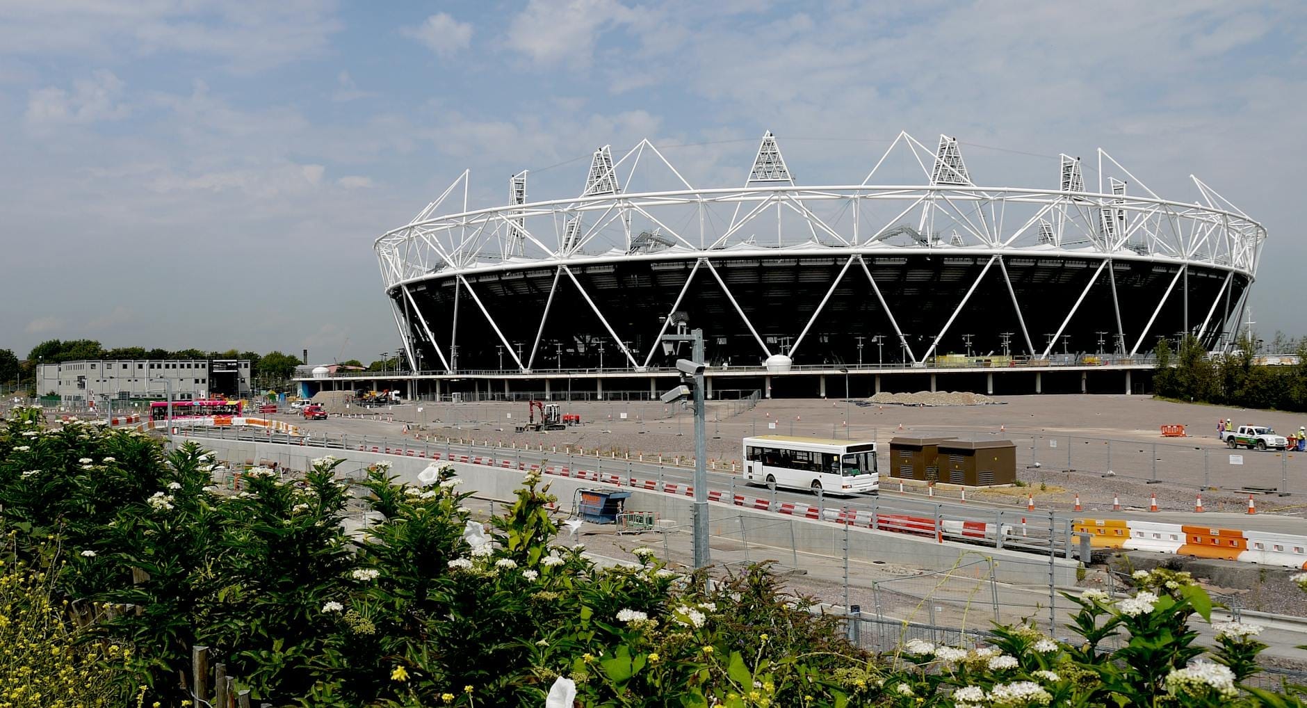 Vista panoramica del London Olympic Stadium circondato da spazio aperto, verde e barriere di cantiere in una giornata luminosa al Queen Elizabeth Olympic Park.
