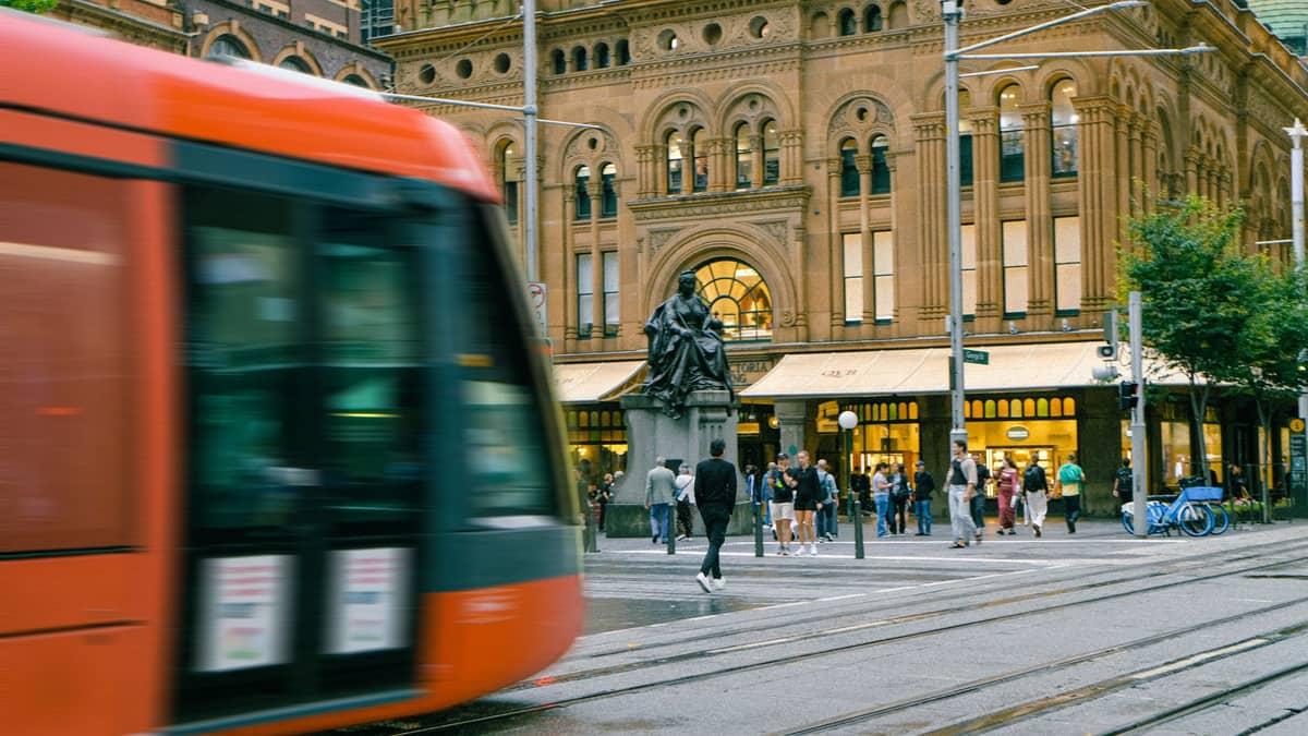 L'ingresso principale del Queen Victoria Building di Sydney, con la dettagliata facciata in arenaria, la statua della Regina Vittoria e il vivace traffico della città con un tram in primo piano.