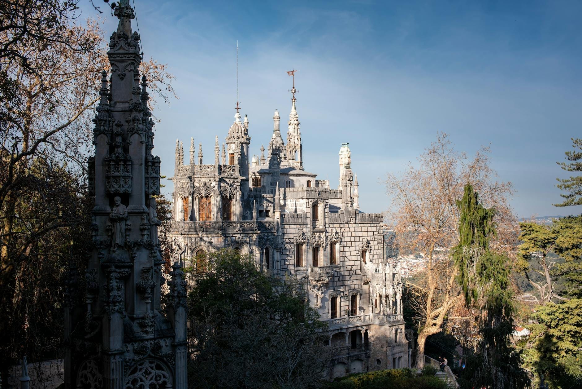 Vista panoramica del palazzo della Quinta da Regaleira con la sua elaborata architettura neogotica, immerso nei rigogliosi giardini sotto un cielo azzurro a Sintra, Portogallo.