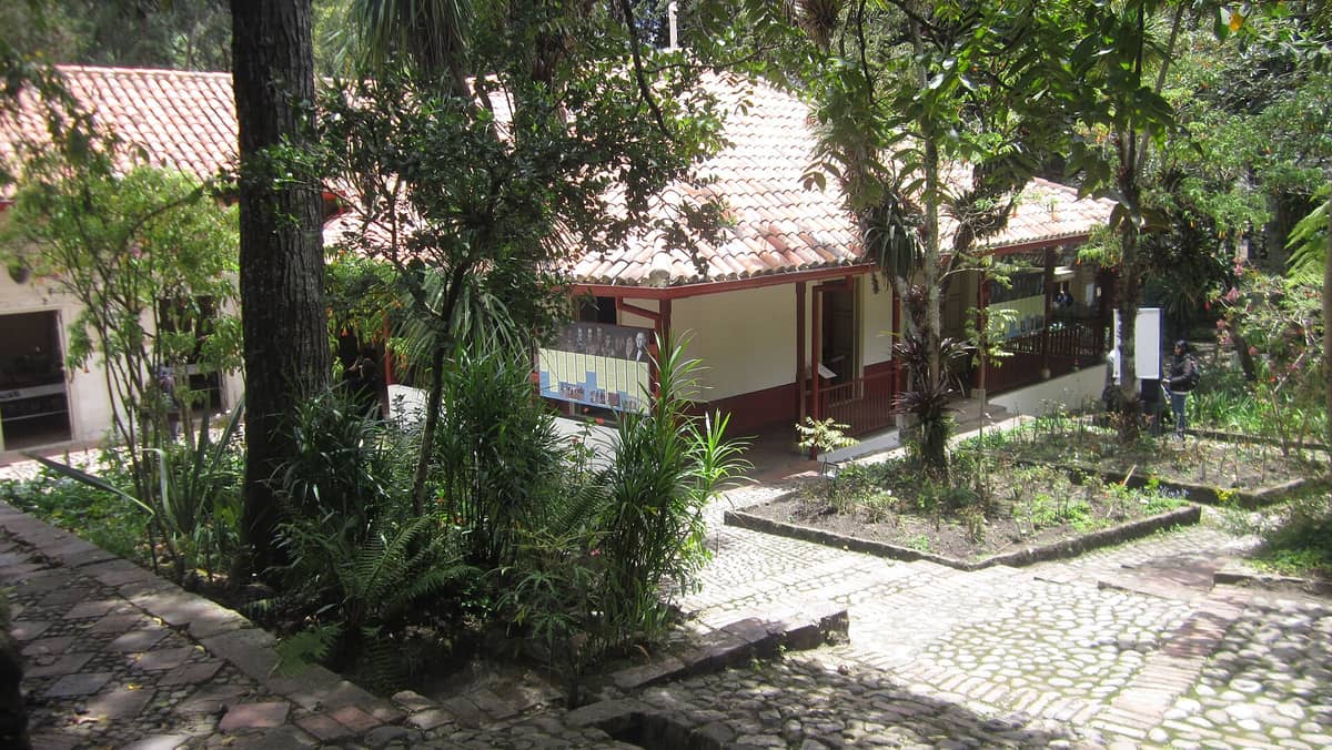 View of the historic Quinta de Bolívar estate in Bogotá, showing a traditional colonial house with red tile roof, surrounded by lush gardens and trees.