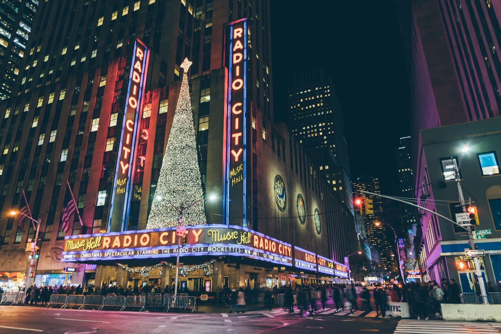 Vista notturna della Radio City Music Hall a Midtown Manhattan con le sue iconiche insegne al neon, la marquee Art Déco e un grande albero di Natale illuminato all'esterno.