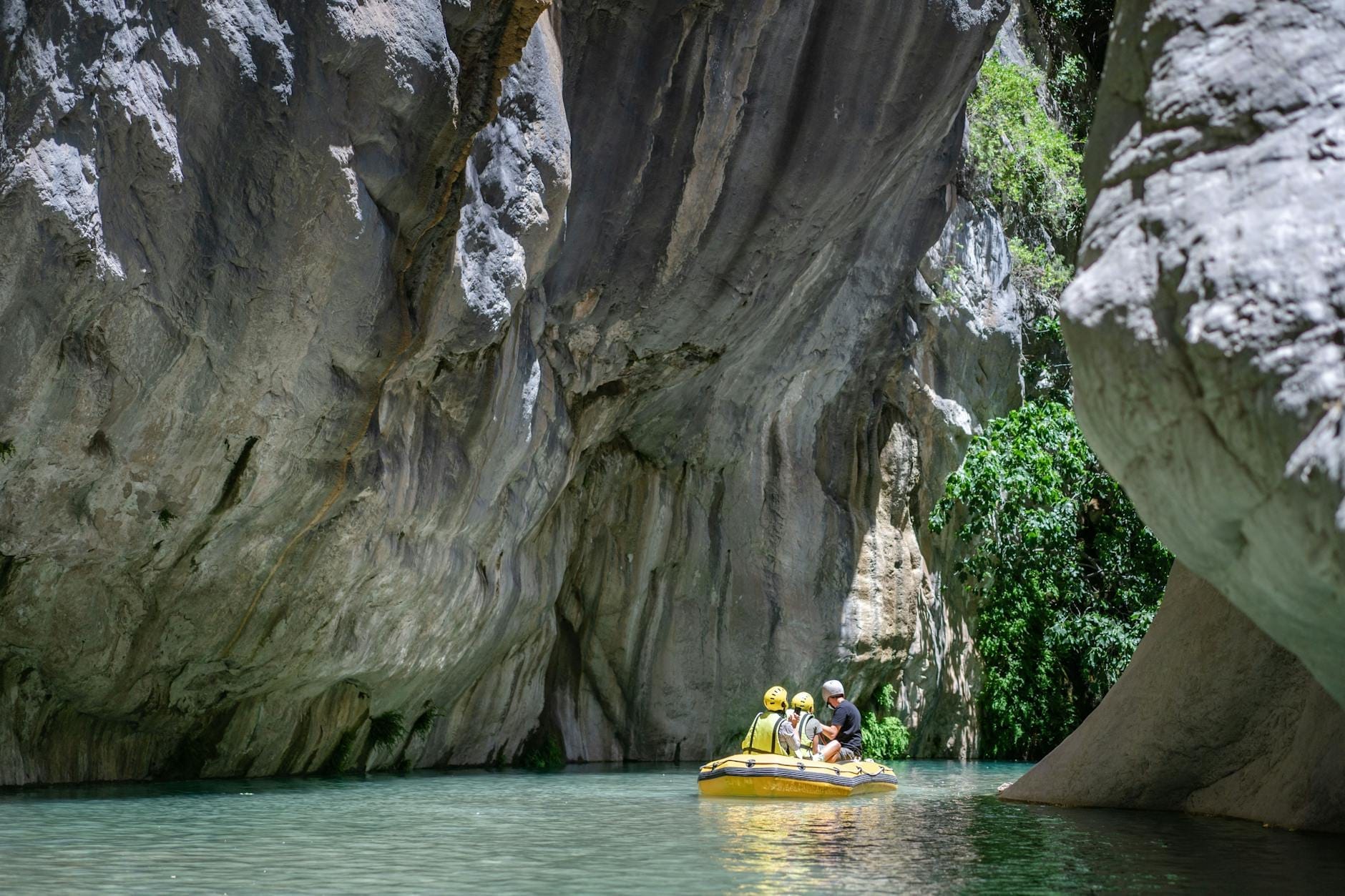 Um pequeno grupo fazendo rafting pelas falésias dramáticas e águas turquesa do Cânion Köprülü, cercado por vegetação exuberante e formações rochosas.