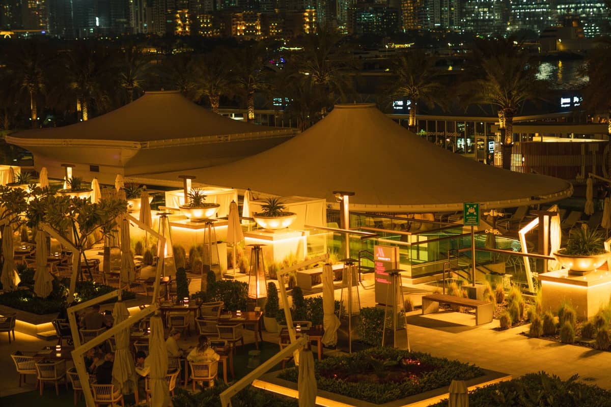 Outdoor-Bar und Restaurantterrasse eines Hotels in Dubai bei Nacht, warm beleuchtet mit der Skyline der Stadt im Hintergrund und gedeckten Tischen für die Gäste.