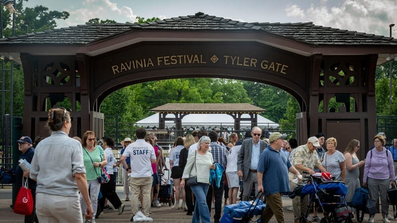 I visitatori entrano attraverso il cancello in legno Ravinia Festival Tyler Gate, circondato da alberi e nuvole, con folle che portano sedie da prato e forniture per picnic.