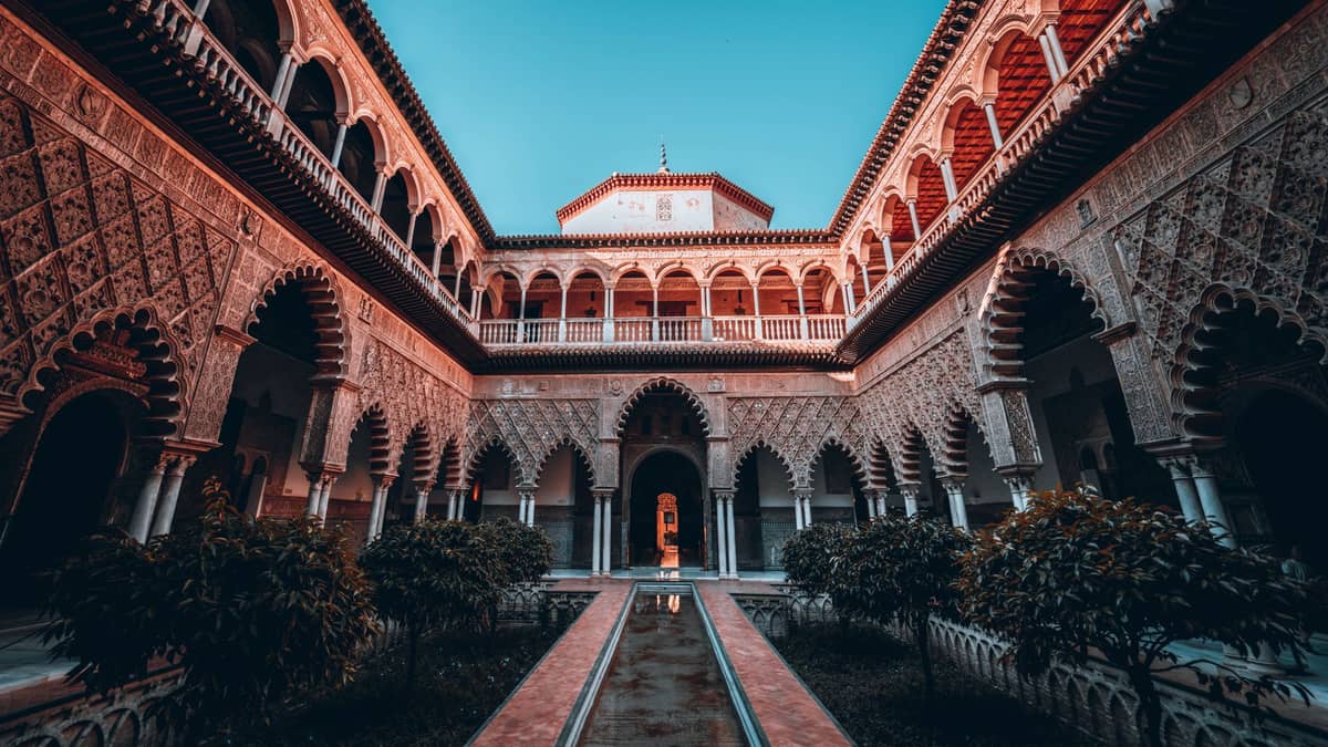 วิวกว้างของลาน Patio de las Doncellas อันโด่งดังใน Real Alcázar de Sevilla ที่โดดเด่นด้วยซุ้มโค้งมัวร์ สระน้ำกลาง และต้นส้มร่มรื่น