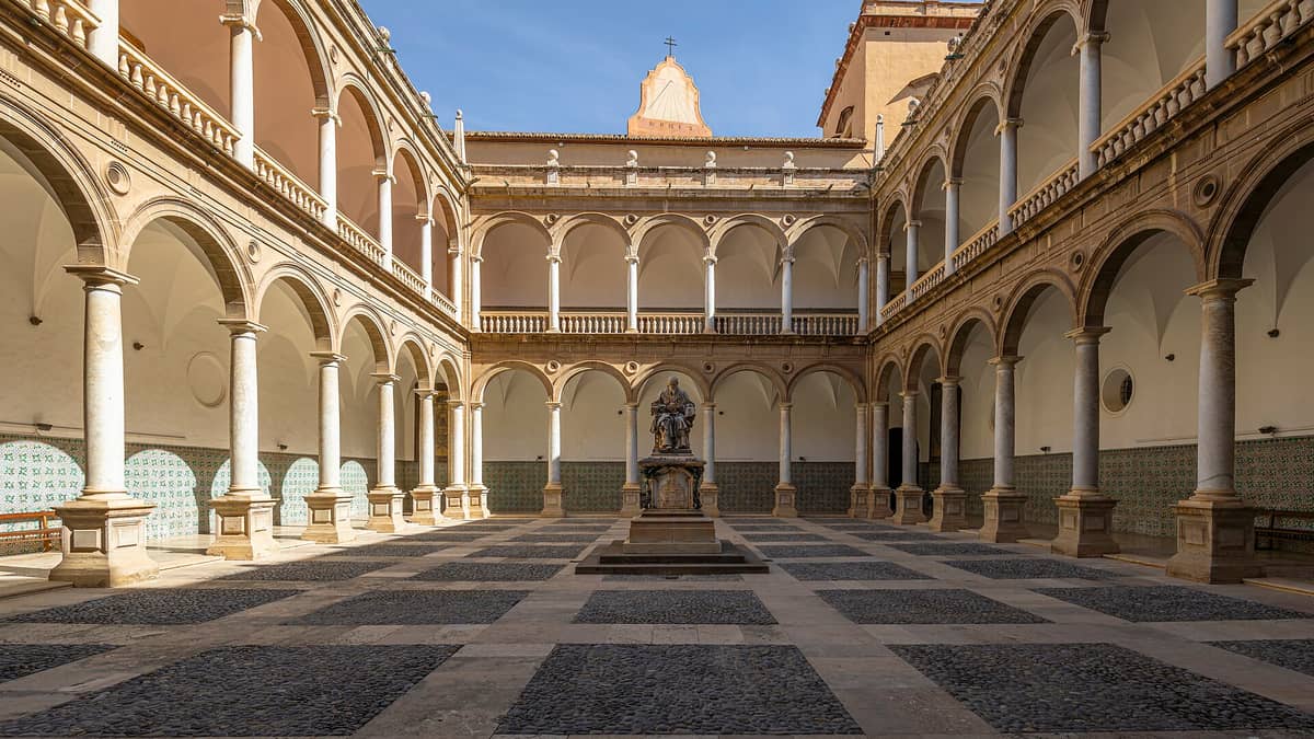 Vista panoramica del chiostro rinascimentale del Real Colegio Seminario del Corpus Christi a Valencia, con doppie arcate, colonne in marmo e una statua centrale immersa nella luce del sole.