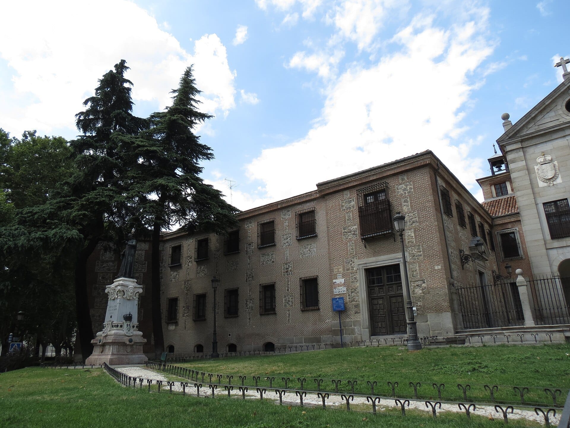 Facciata in mattoni del Real Monasterio de la Encarnación a Madrid, con una statua e un lussureggiante prato verde sotto un cielo azzurro brillante.
