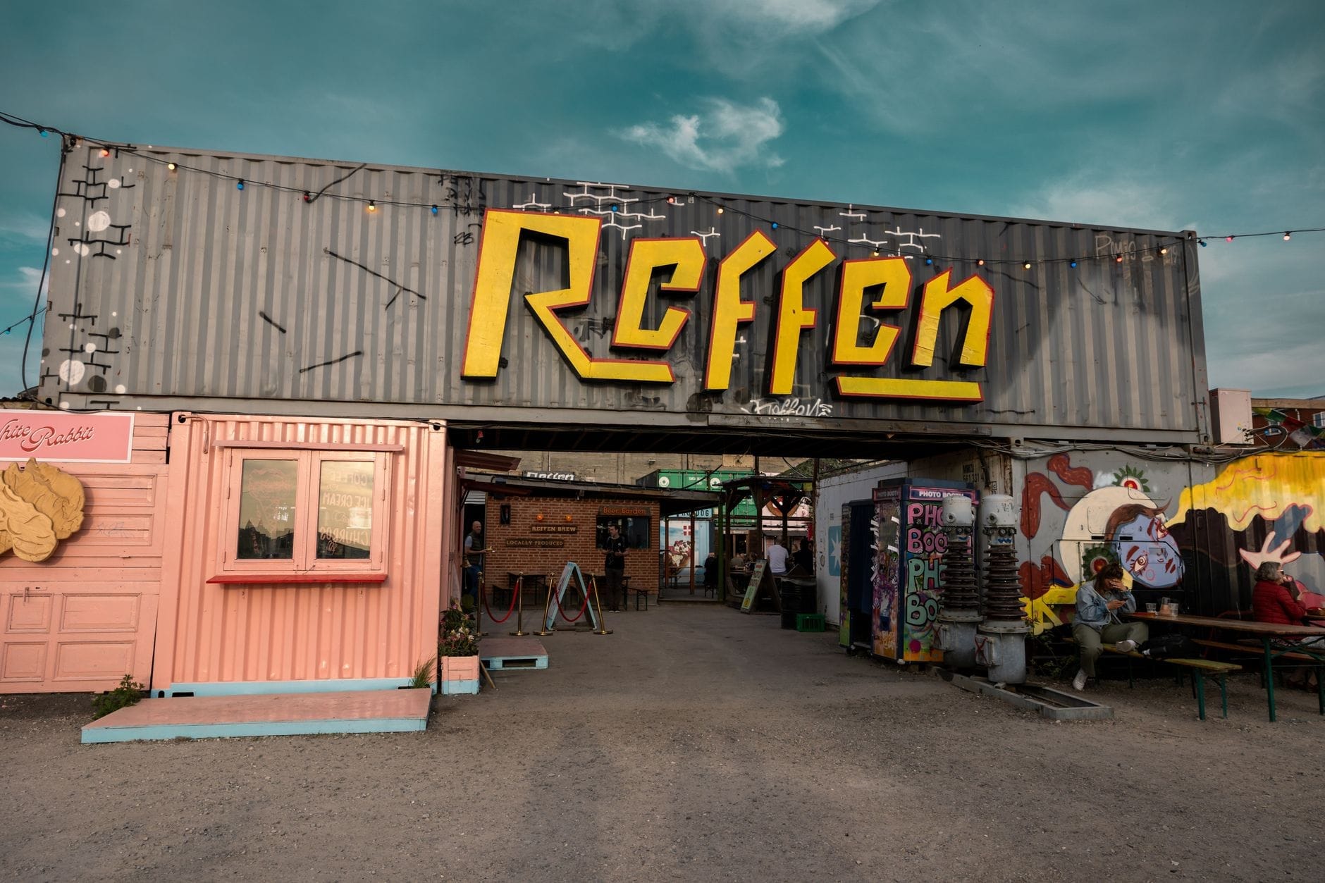 Vista dell'ingresso principale del mercato di street food Reffen con l'insegna gialla, i colorati container marittimi e i posti a sedere all'aperto in una giornata di sole.