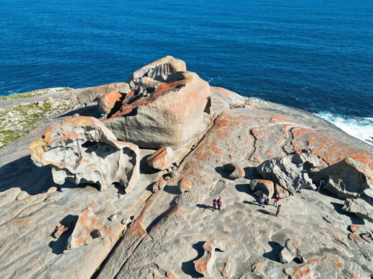 Aerial view of Remarkable Rocks, showcasing uniquely shaped granite boulders on Kangaroo Island with people for scale and the Southern Ocean in the background.