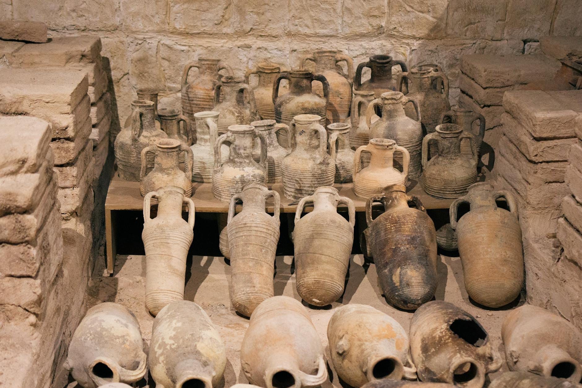 Esposizione di numerose anfore e ceramiche minoiche in argilla disposte su scaffali davanti a una parete di pietra all'interno di un museo archeologico.