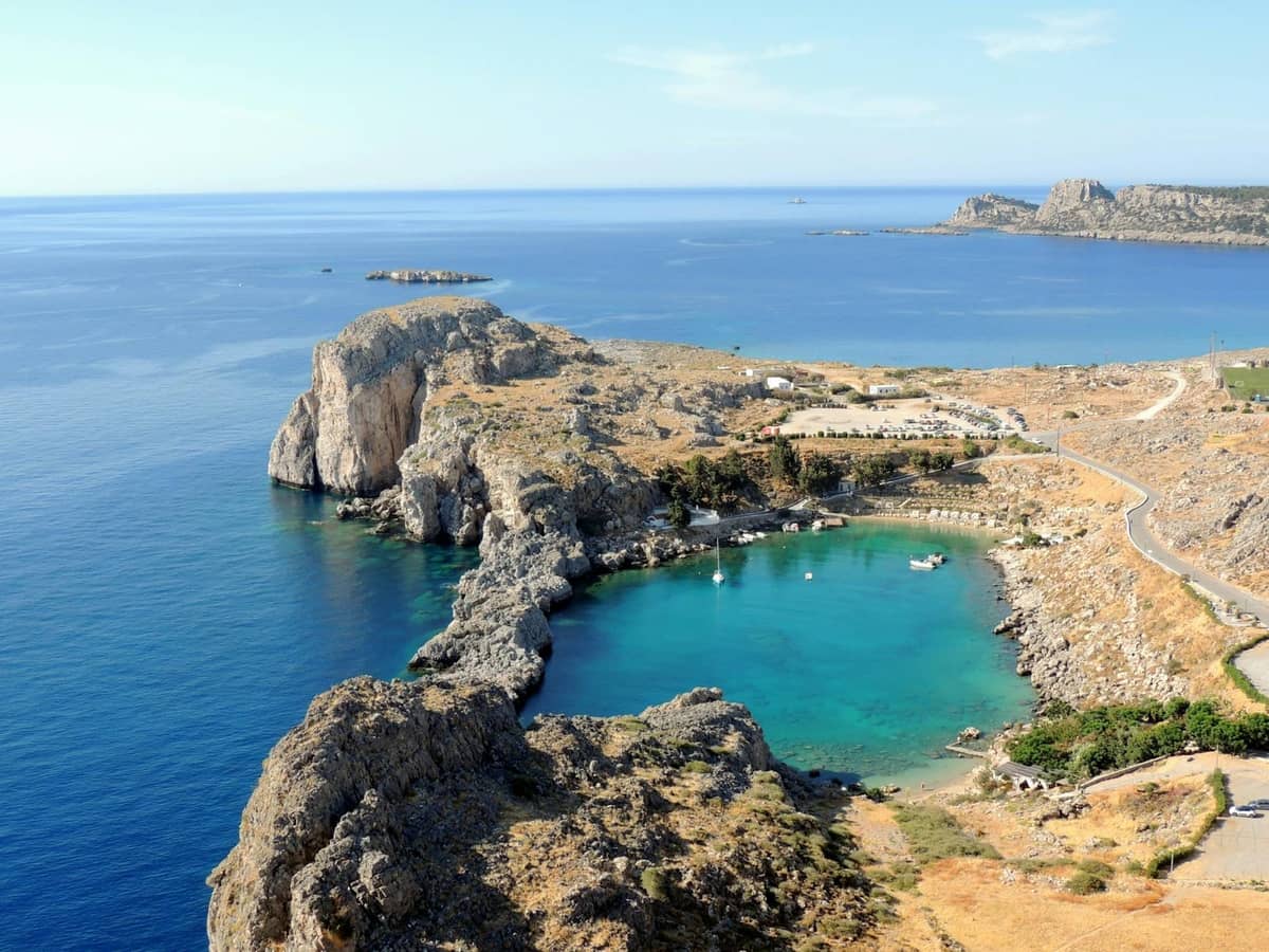 A quiet rocky bay with turquoise water and sparse visitors, surrounded by dramatic coastal cliffs on the island of Rhodes.