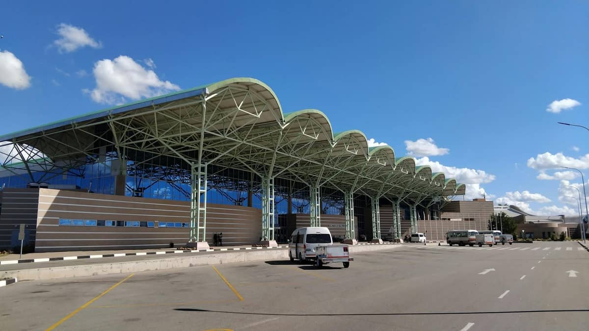 Exterior of Rhodes International Airport with distinctive wavy roof and taxis waiting outside under a clear blue sky.