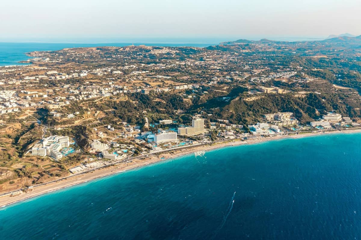 Aerial view of Rhodes coastline with hotels, town buildings, and deep blue sea under clear sky
