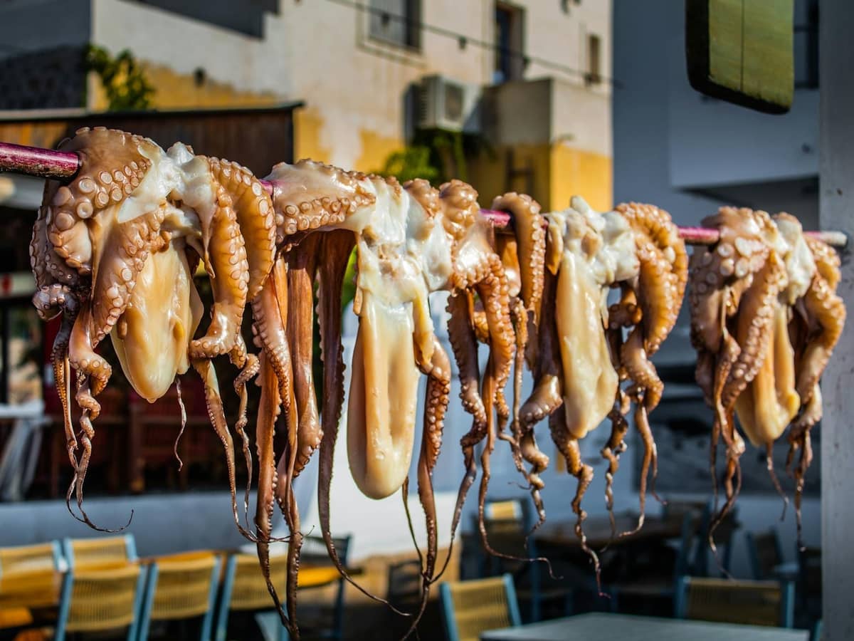 Fresh octopus hanging to dry outside a seafood taverna in Rhodes, with tables and chairs in the background.