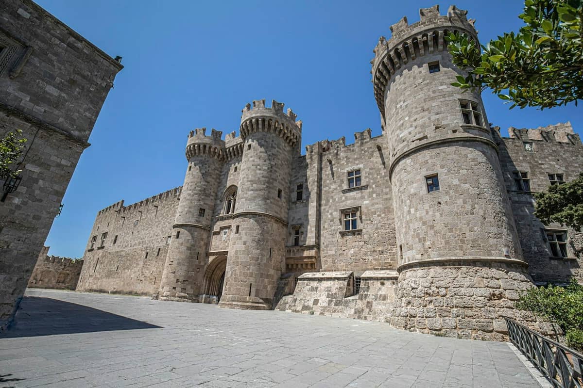 Imposing medieval stone castle with round towers and battlements under blue sky in Rhodes, Greece.