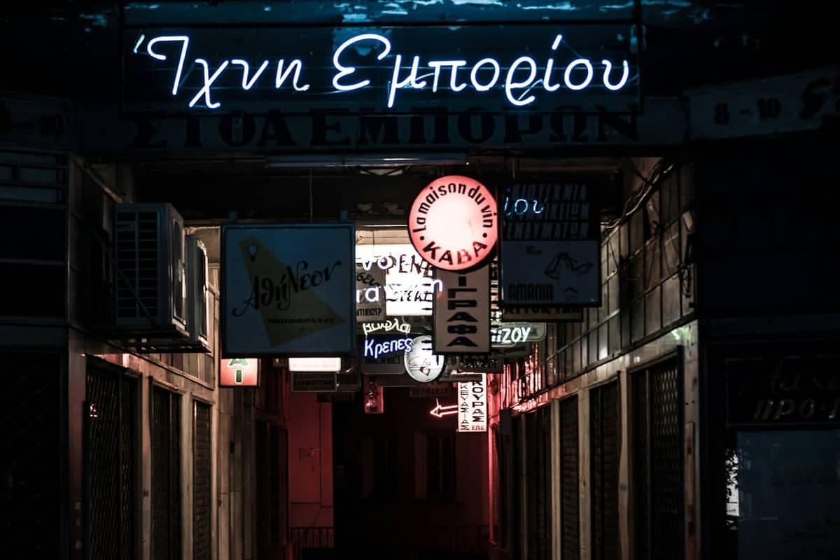 Dimly lit Greek signs and bar decorations in a narrow street at night, capturing the atmosphere of Rhodes nightlife.