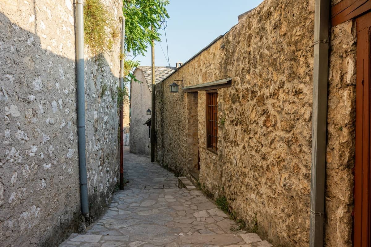 Narrow stone alley with traditional budget guesthouse buildings, sunlight casting shadows in an old town area of Rhodes.