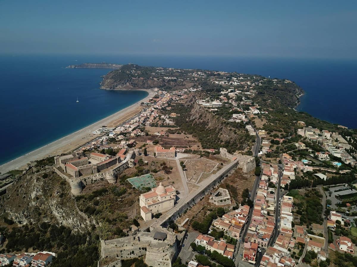 Aerial view of Rhodes town peninsula, with sandy beach, historic walls, and blue sea surrounded by buildings.