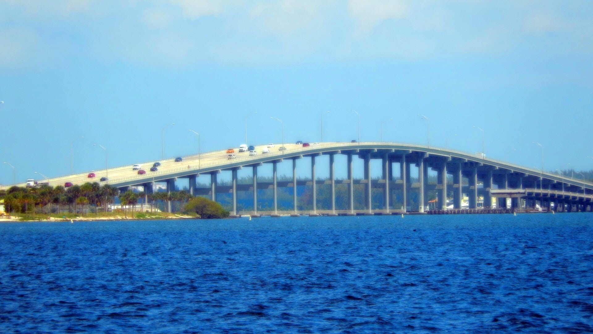Rickenbacker Causeway che attraversa la Baia di Biscayne con veicoli in transito, circondato da acqua blu e palme sotto un cielo sereno.
