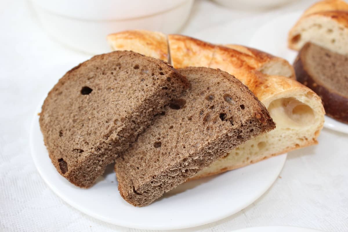 Teller mit Scheiben von dichtem, dunklem Roggenbrot und hellerem Brot, Nahaufnahme auf weißem Tischtuch.