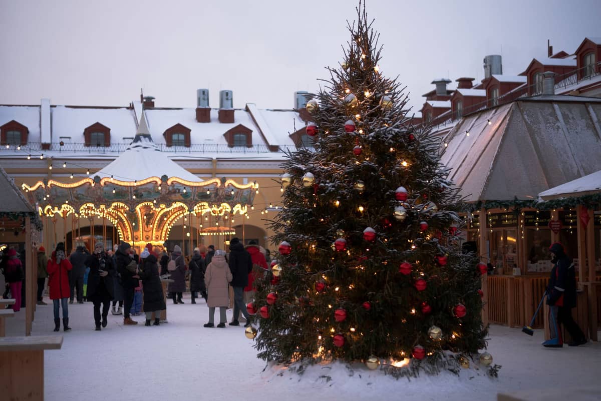 Weihnachtsmarkt im Freien im Winter mit geschmücktem Baum, Karussell, Ständen und einkaufenden Menschen auf einem verschneiten europäischen Platz.
