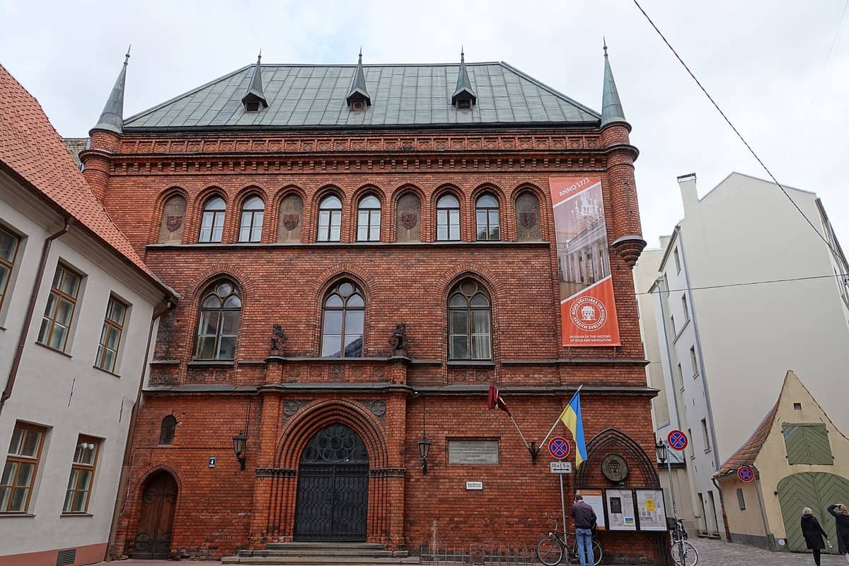 Frontansicht des Museums für die Geschichte Rigas und die Schifffahrt mit seinem historischen roten Backsteingebäude, gotischen Bogenfenstern und Museumsbannern.