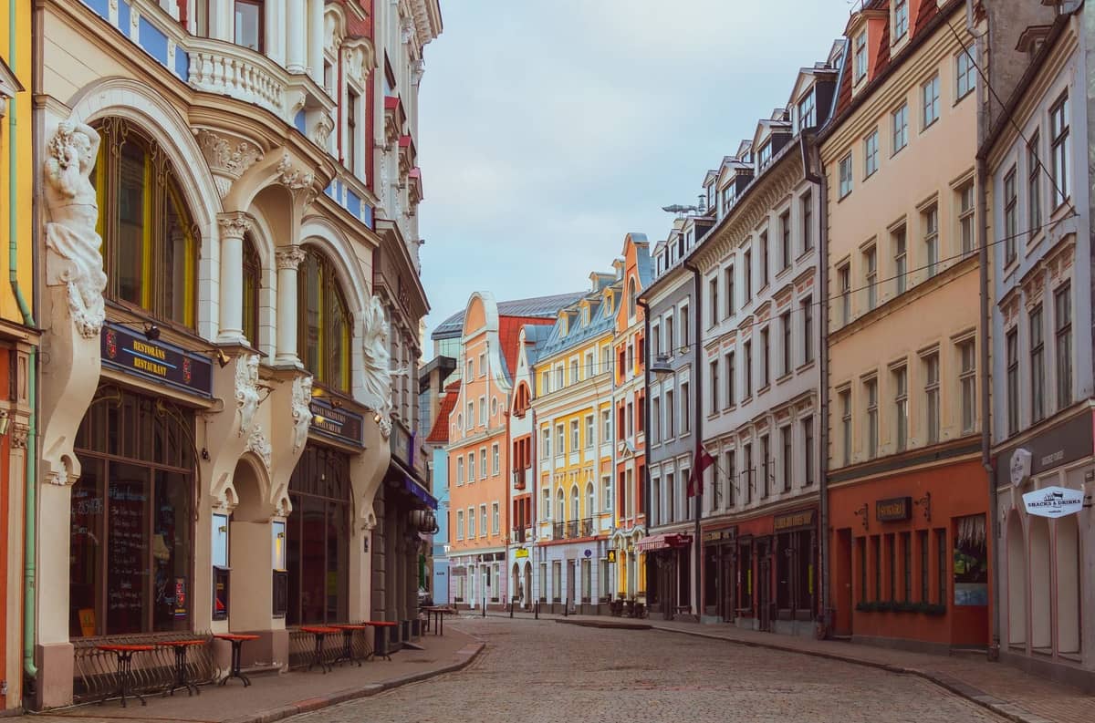 Breite Kopfsteinpflasterstraße gesäumt von verzierten historischen Gebäuden in der Altstadt von Riga, die den unebenen Untergrund zeigt, der für Gehtipps relevant ist.