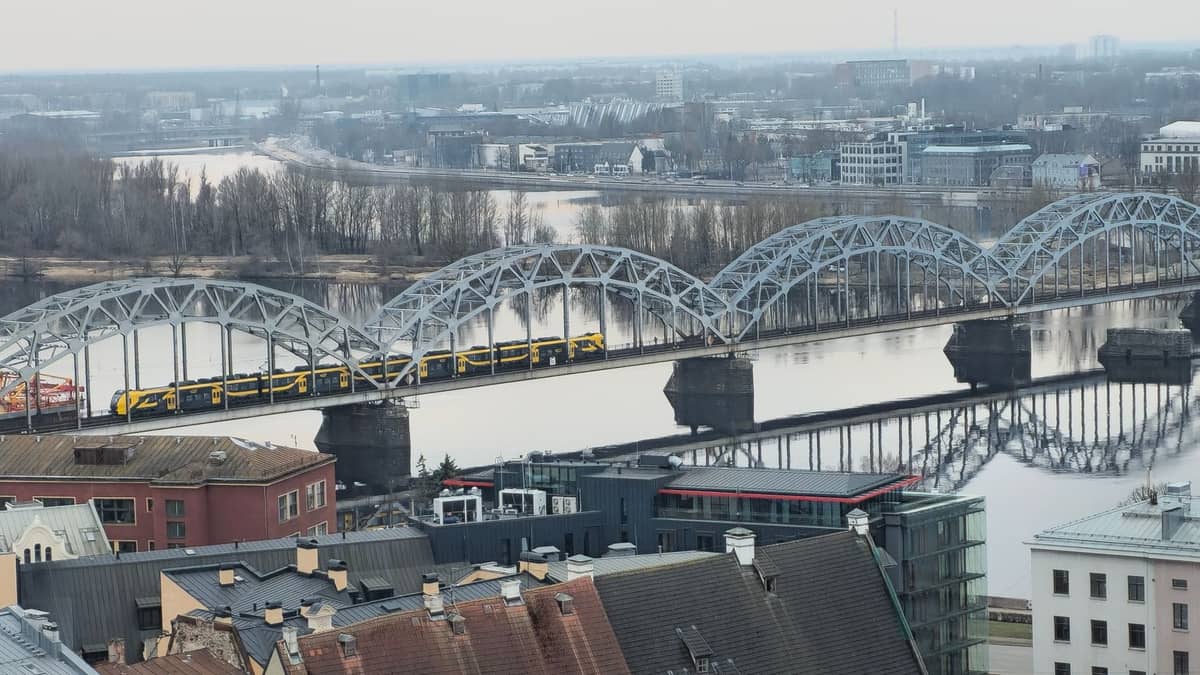 Blick auf die Stadt Riga mit der ikonischen Eisenbahnbrücke über die Daugava, moderne Gebäude und Wohnhausdächer sichtbar