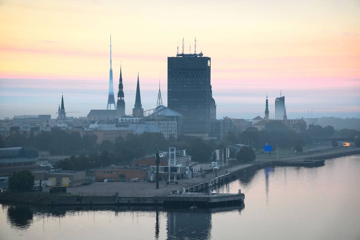 Eine stimmungsvolle Stadtansicht von Riga mit dem schwarzen, rechteckigen Gebäude der Latvian Academy of Sciences zwischen Kirchturmspitzen bei Sonnenaufgang.