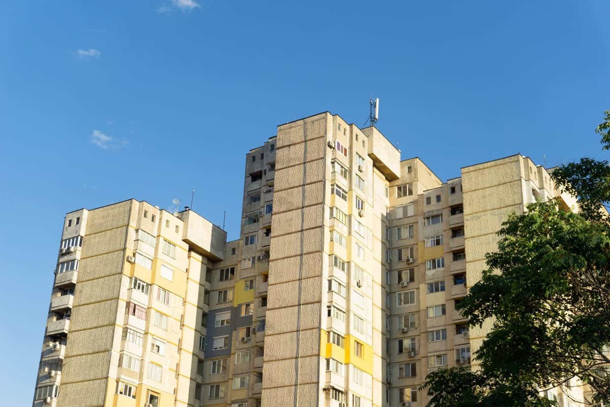 Plattenbau-Wohnblock aus der Sowjetzeit mit gelber und beiger Fassade unter klarem blauem Himmel mit Baumästen im Vordergrund