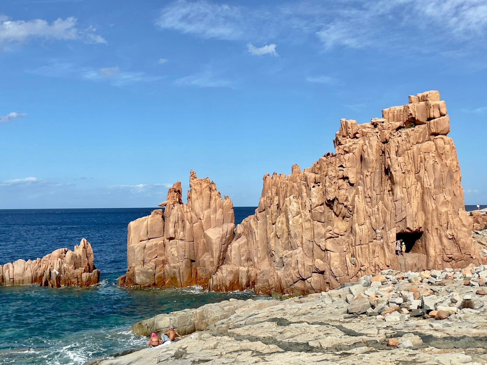 Die markanten roten Porphyrfelsen von Rocce Rosse di Arbatax ragen steil über das blaue Tyrrhenische Meer unter einem hellen, klaren Himmel empor.