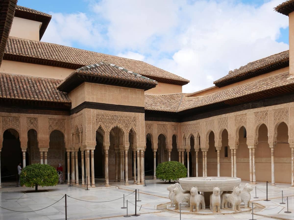 ลานกลางแจ้งของ Patio de los Leones ใน Alhambra พร้อมระเบียงโค้งที่ประณีต น้ำพุกลางลาน และท้องฟ้าแดดจ้า
