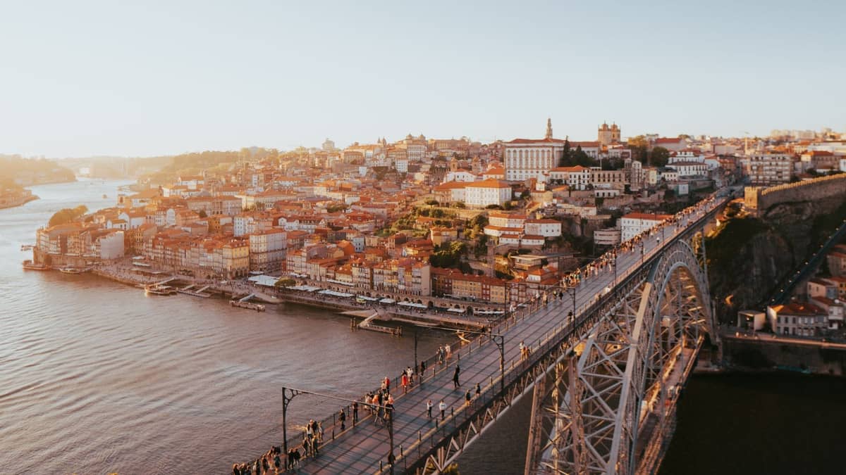 Vista aérea del Puente Dom Luís I sobre el río Douro al atardecer, con personas caminando por el puente y el histórico paisaje urbano de Porto al fondo.
