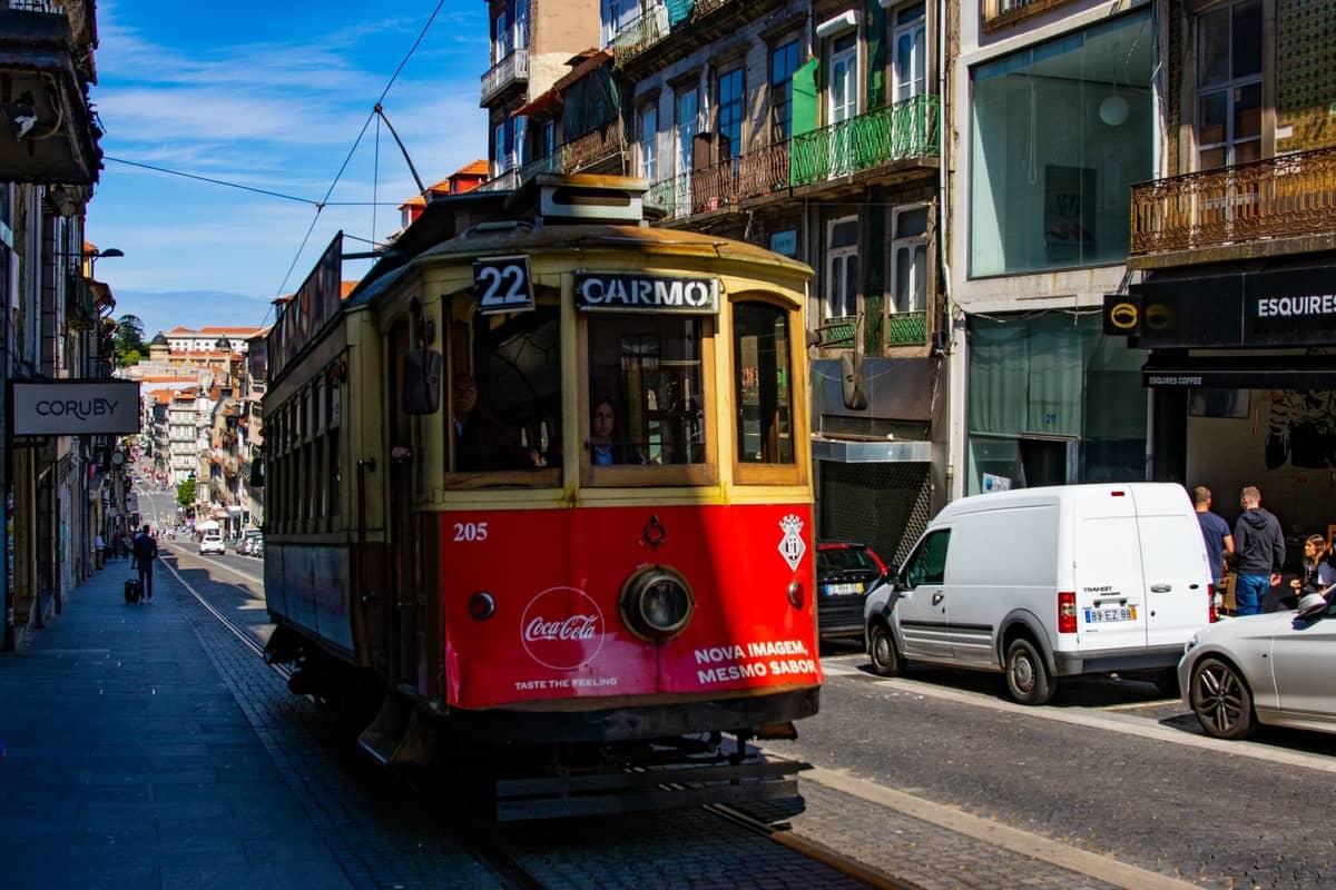 Tranvía histórico de la línea 22 subiendo por una colorida calle del centro de Porto, con peatones y edificios antiguos bajo la luz del día.