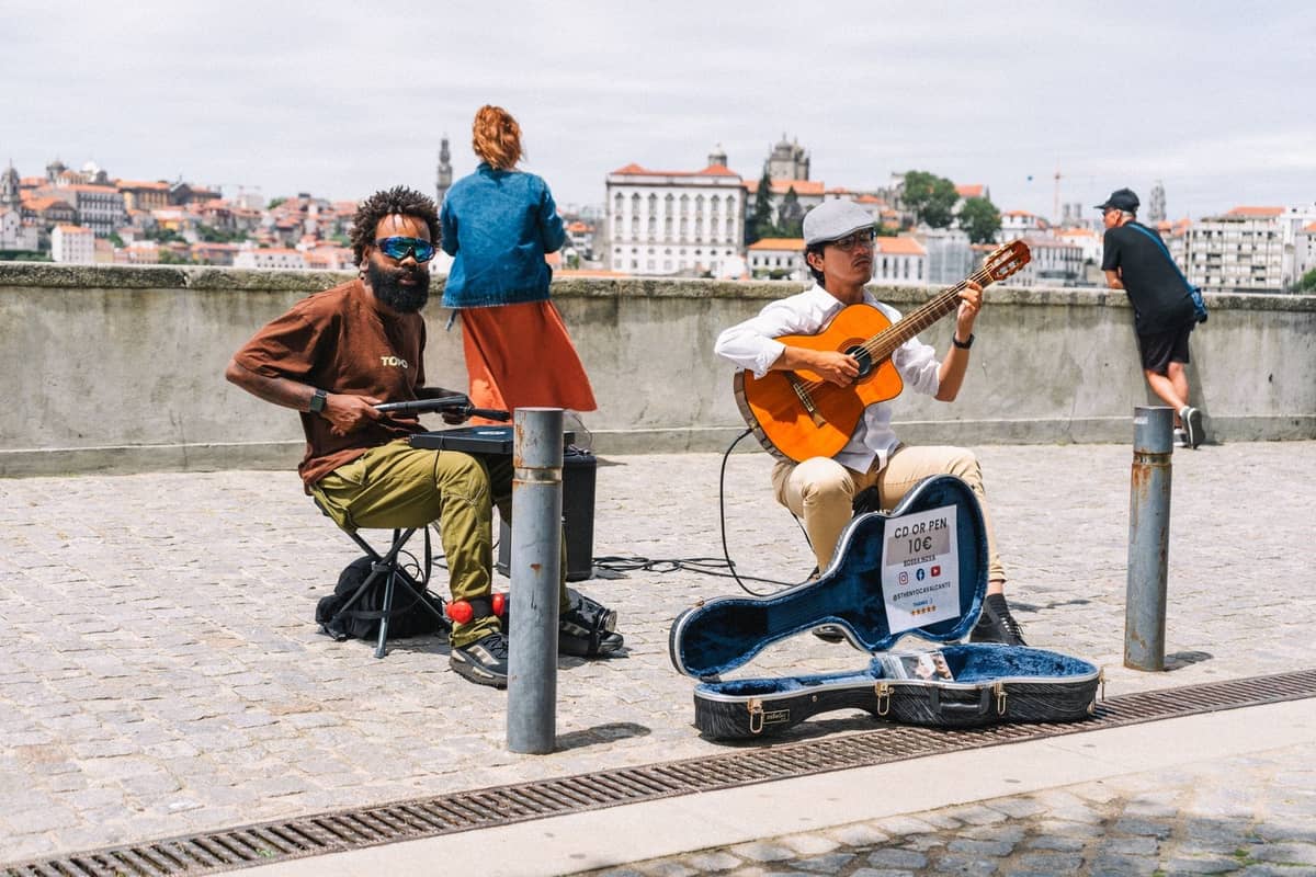 Dos músicos actúan al aire libre junto al río Duero en Oporto, con el paisaje urbano visible al fondo.