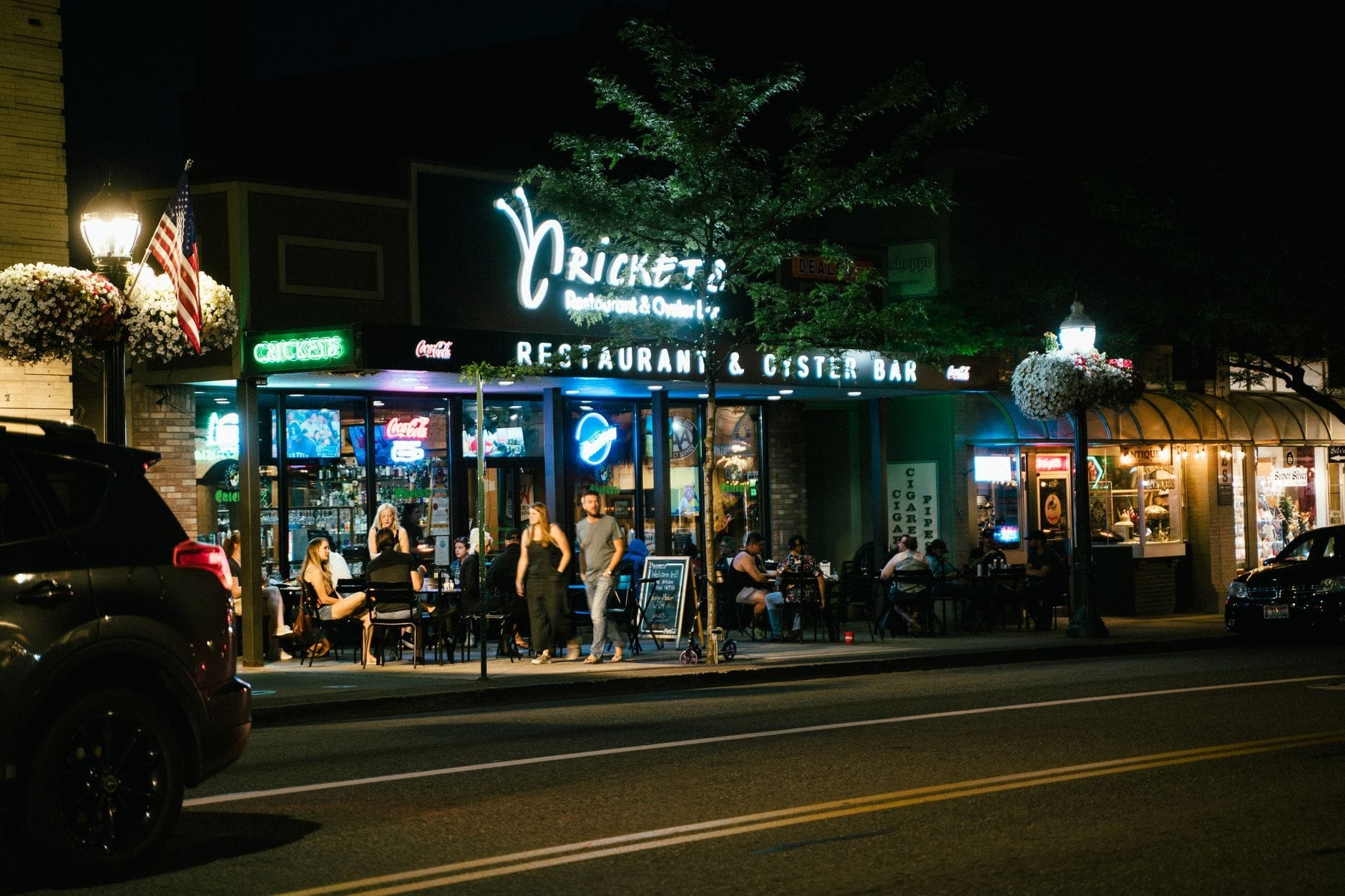 Vista nocturna de personas cenando al aire libre en Cricket's Restaurant & Oyster Bar en Nashville, con letreros de neón brillantes y un ambiente relajado y acogedor.