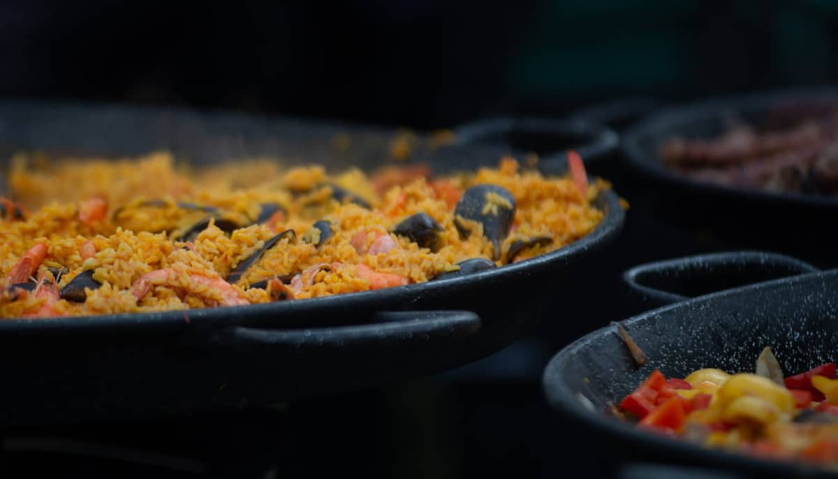 Gros plan d'une poêle à paella traditionnelle avec du riz fumant, des crevettes et des moules, évoquant un repas à Valence, Espagne.