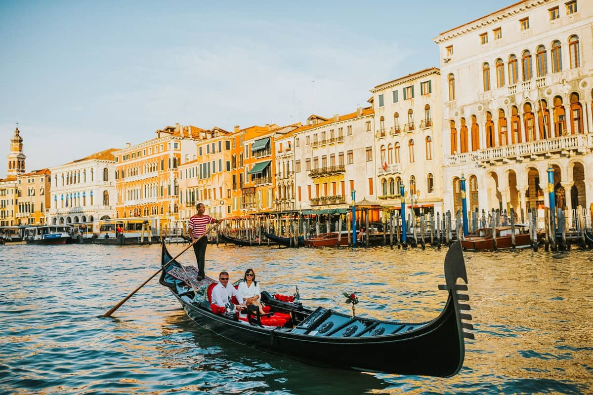 Gondoliere steuert eine Gondel mit einem Pärchen durch den Canal Grande mit venezianischen Gebäuden im Hintergrund