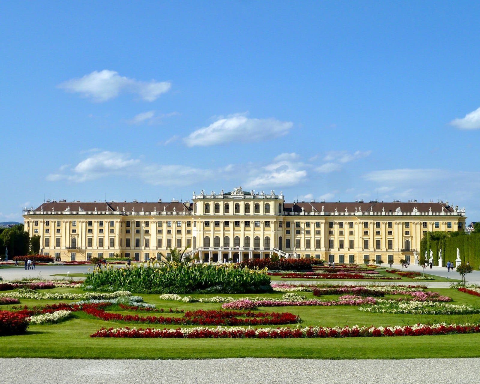 Weitblick auf das Schloss Schönbrunn in Wien mit symmetrischen Gärten und strahlend blauem Himmel.