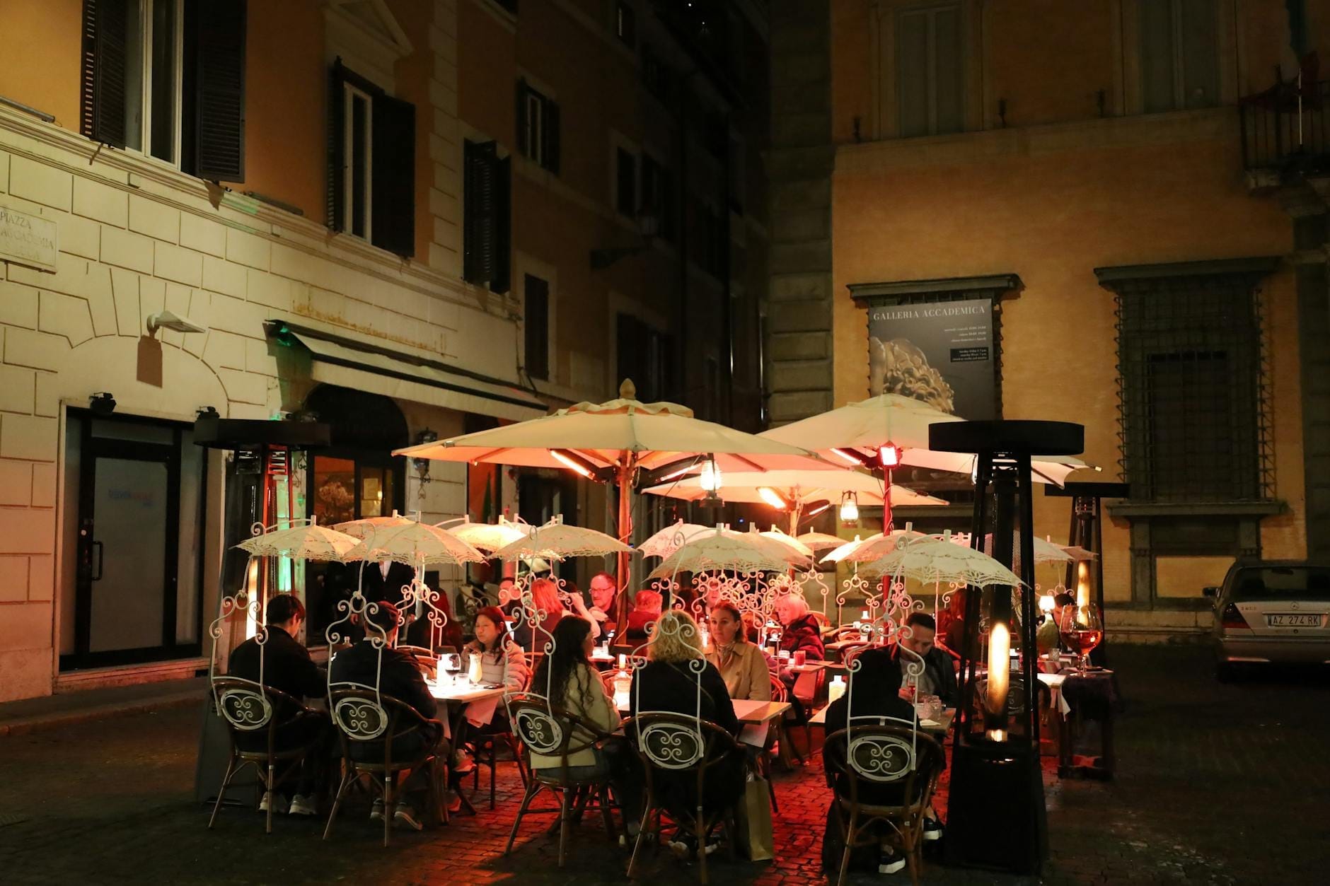 Outdoor restaurant in Rome at night with people dining under umbrellas, warm lighting, and historic buildings in the background.